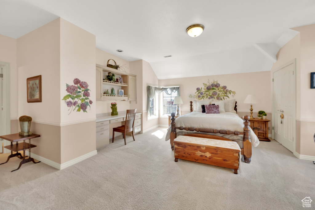 Bedroom with built in desk, light colored carpet, and lofted ceiling
