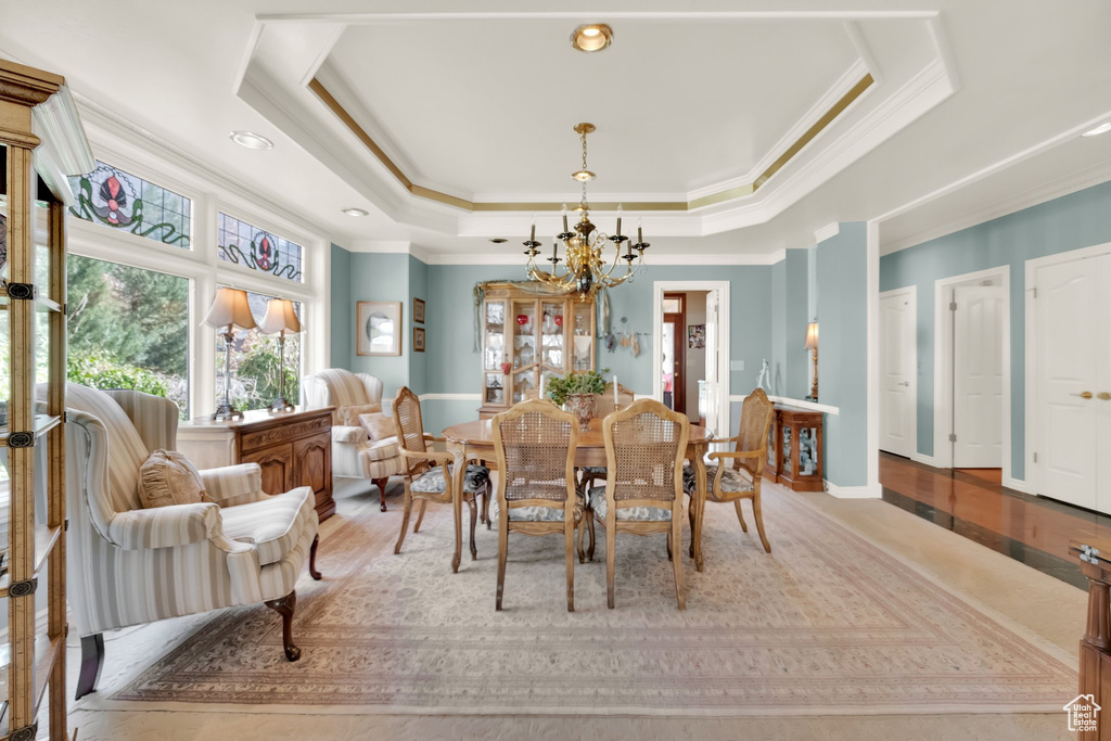 Dining room with crown molding, a chandelier, a raised ceiling, and light wood finished floors