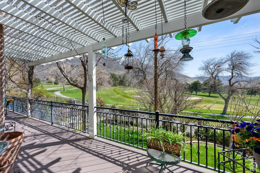 Wooden deck with view of golf course, a mountain view, and a pergola
