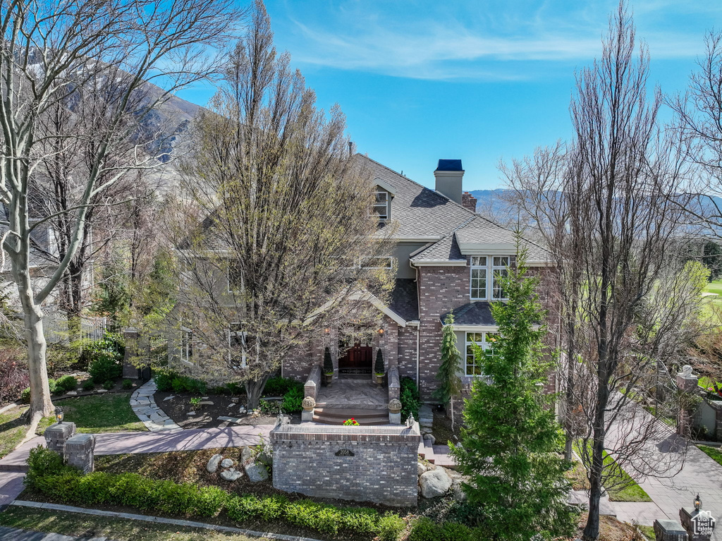 View of front of house featuring a chimney, a mountain view, brick siding, and a shingled roof