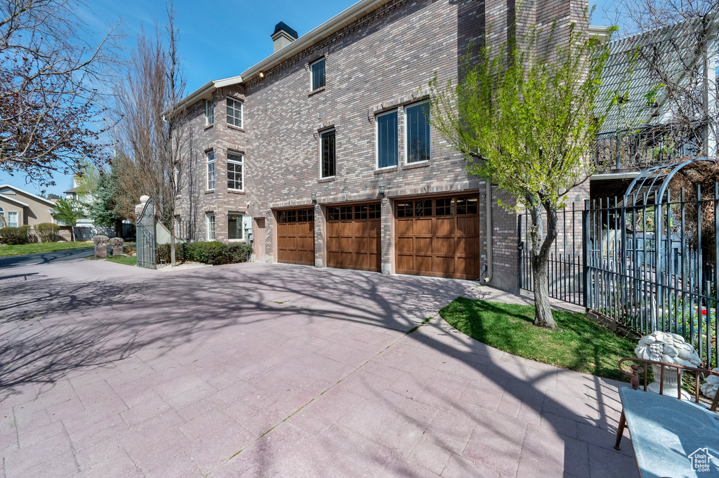 Rear view of house featuring an attached garage, concrete driveway, brick siding, and a chimney