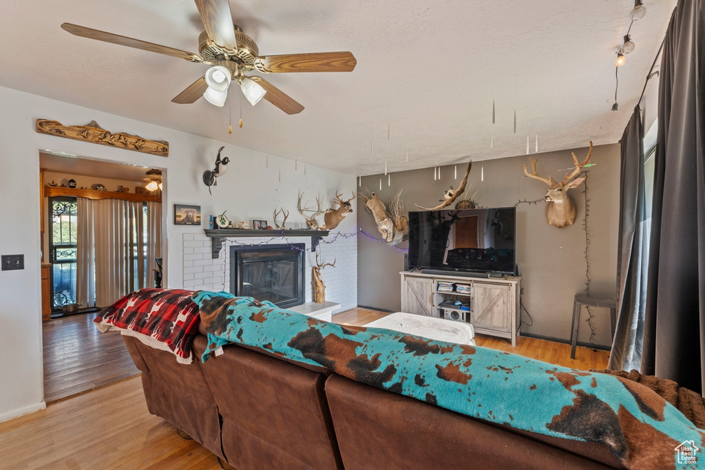 Living area featuring light wood-type flooring, a brick fireplace, and ceiling fan