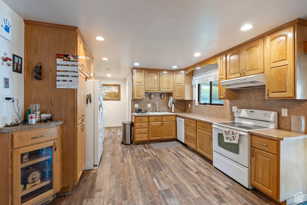 Kitchen featuring white appliances, under cabinet range hood, wood finished floors, tasteful backsplash, and recessed lighting