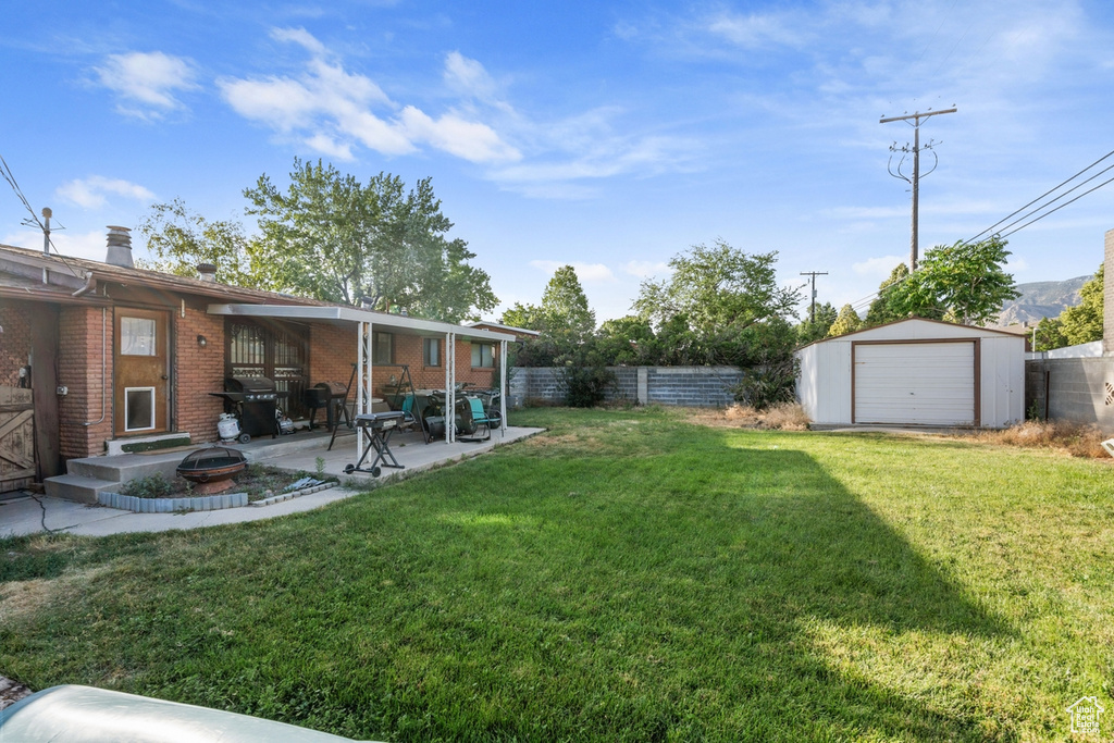 Fenced backyard featuring a patio area, a detached garage, a storage unit, and a fire pit