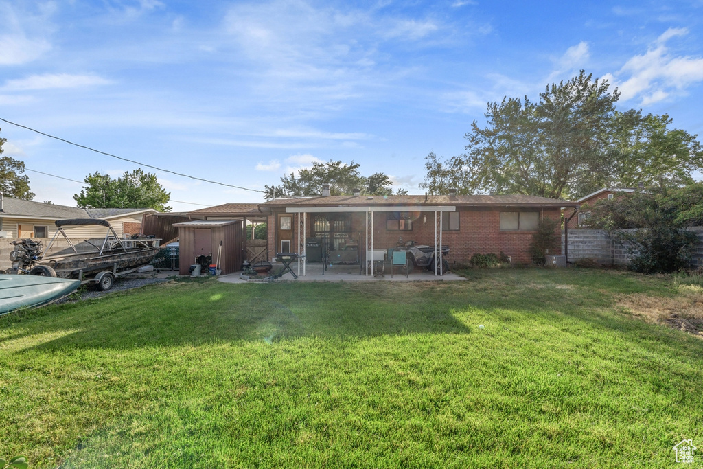 Rear view of house with a storage unit, a patio, and brick siding