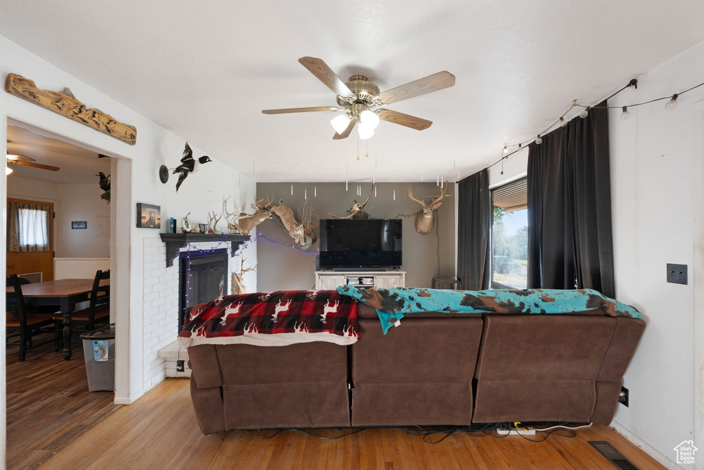 Living room with a ceiling fan, wood finished floors, and a fireplace
