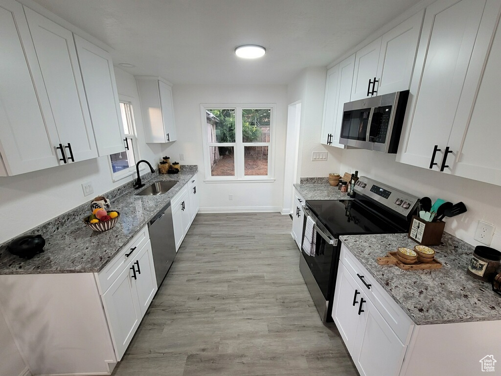 Kitchen with stainless steel appliances, light wood-style flooring, white cabinetry, and light stone counters