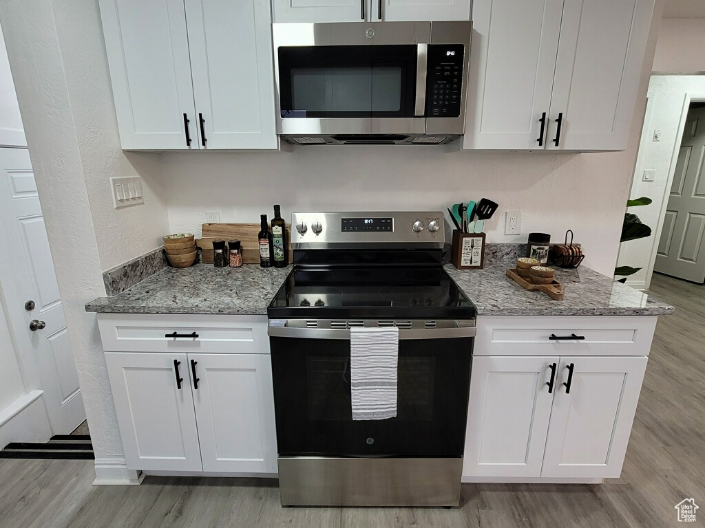 Kitchen with appliances with stainless steel finishes, light wood finished floors, and white cabinetry