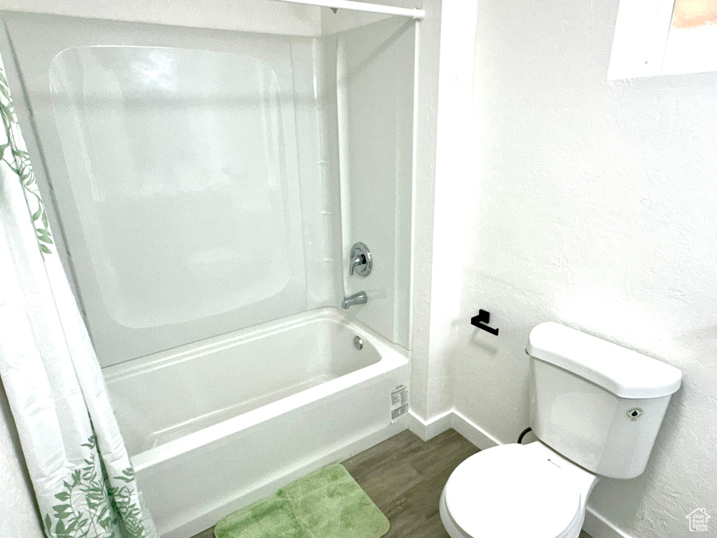 Bathroom with wood finished floors, shower / bath combination with curtain, and a textured wall