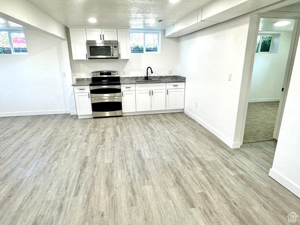 Kitchen featuring stainless steel appliances, white cabinets, light wood-type flooring, and dark stone counters