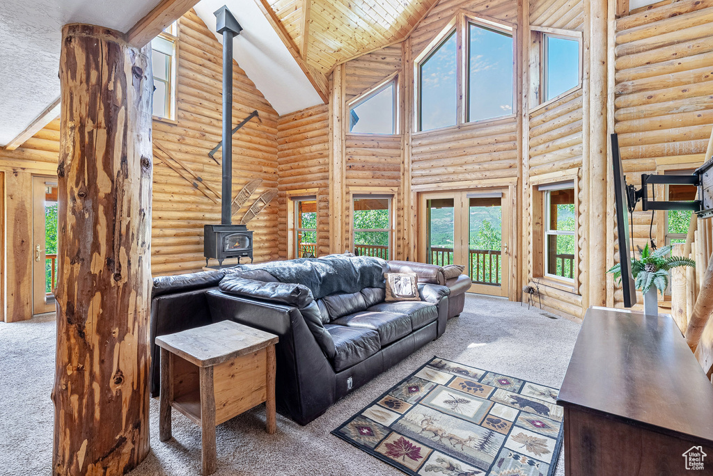 Carpeted living area featuring high vaulted ceiling, a wood stove, rustic walls, and wood ceiling
