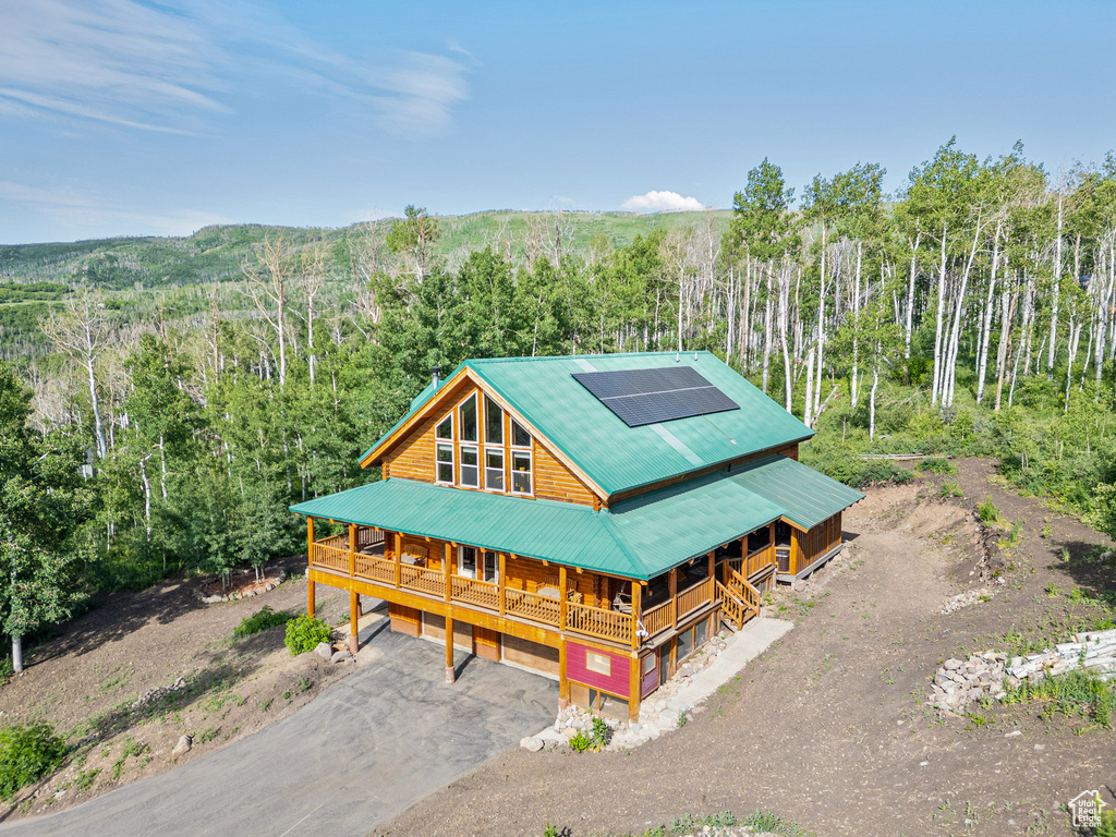 Rustic home with covered porch, a wooded view, solar panels, asphalt driveway, and a metal roof