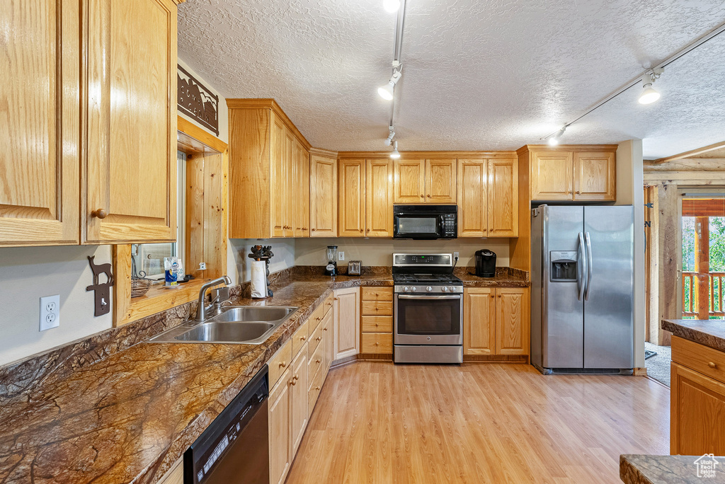 Kitchen with black appliances, rail lighting, light wood-style flooring, dark countertops, and light brown cabinetry