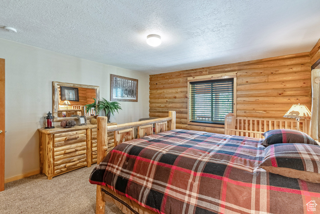 Carpeted bedroom featuring log walls and a textured ceiling