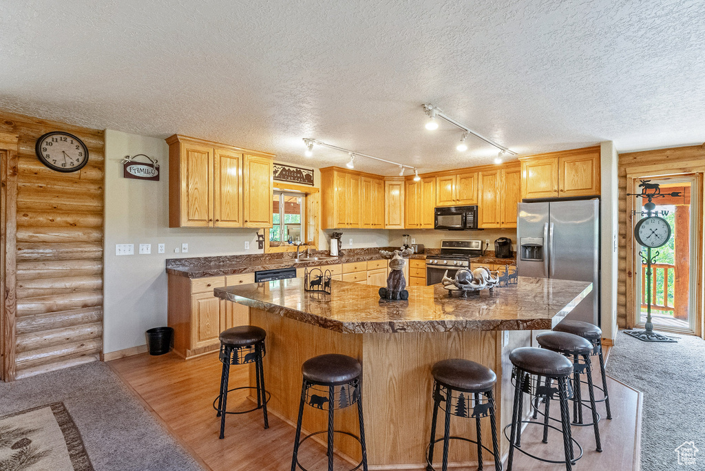 Kitchen with stainless steel appliances, rustic walls, a textured ceiling, a kitchen bar, and a center island
