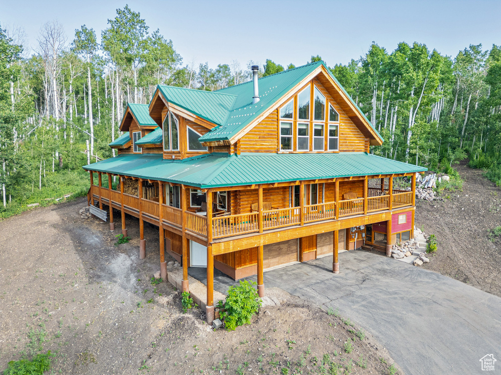 View of front facade with an attached garage, driveway, a metal roof, log siding, and view of wooded area