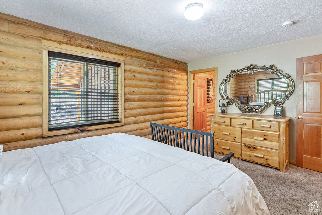 Bedroom with rustic walls, a textured ceiling, and carpet flooring