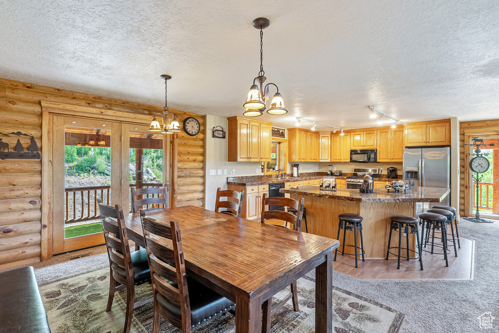 Dining area featuring log walls, a chandelier, a textured ceiling, light carpet, and track lighting