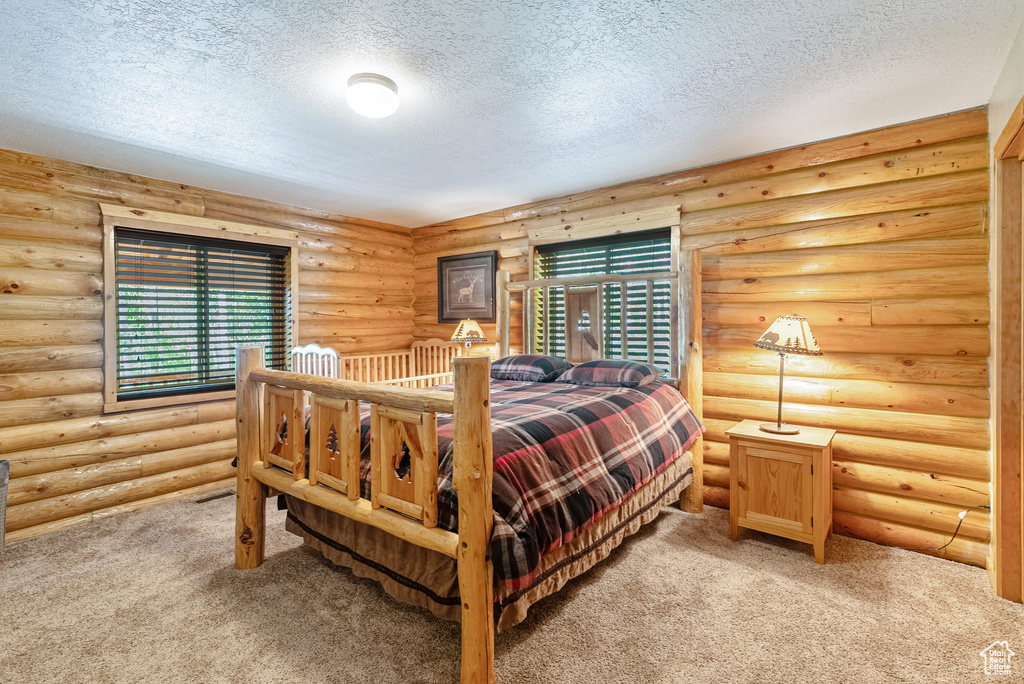 Bedroom featuring a textured ceiling, light colored carpet, and multiple windows