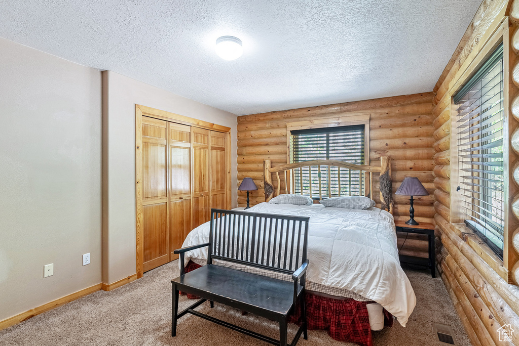 Bedroom with rustic walls, a textured ceiling, carpet, and a closet
