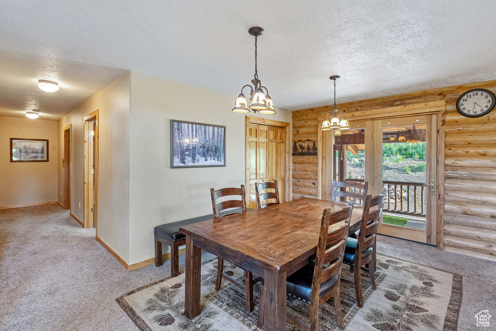 Dining area featuring rustic walls, a textured ceiling, light carpet, and a chandelier