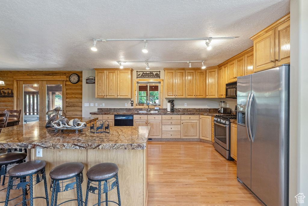 Kitchen featuring black appliances, plenty of natural light, a kitchen bar, light wood finished floors, and a textured ceiling
