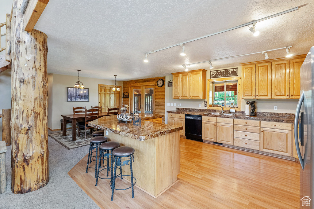Kitchen featuring dishwasher, freestanding refrigerator, a breakfast bar area, light brown cabinets, and light wood-style floors