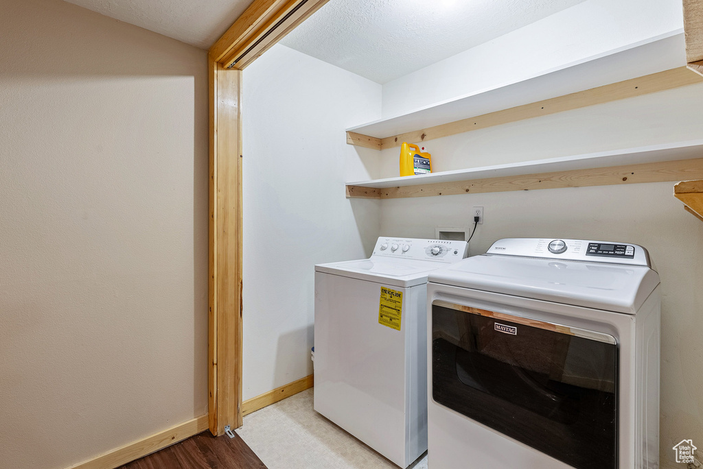 Washroom with washing machine and clothes dryer and light wood-style floors