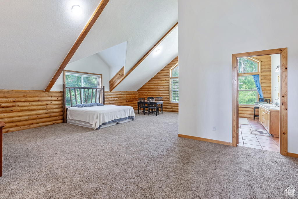 Carpeted bedroom with rustic walls, lofted ceiling, and ensuite bath