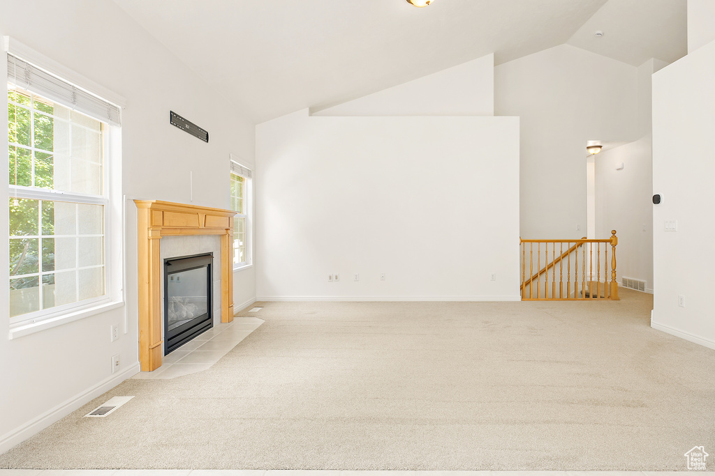 Unfurnished living room with a fireplace, healthy amount of natural light, light colored carpet, and high vaulted ceiling