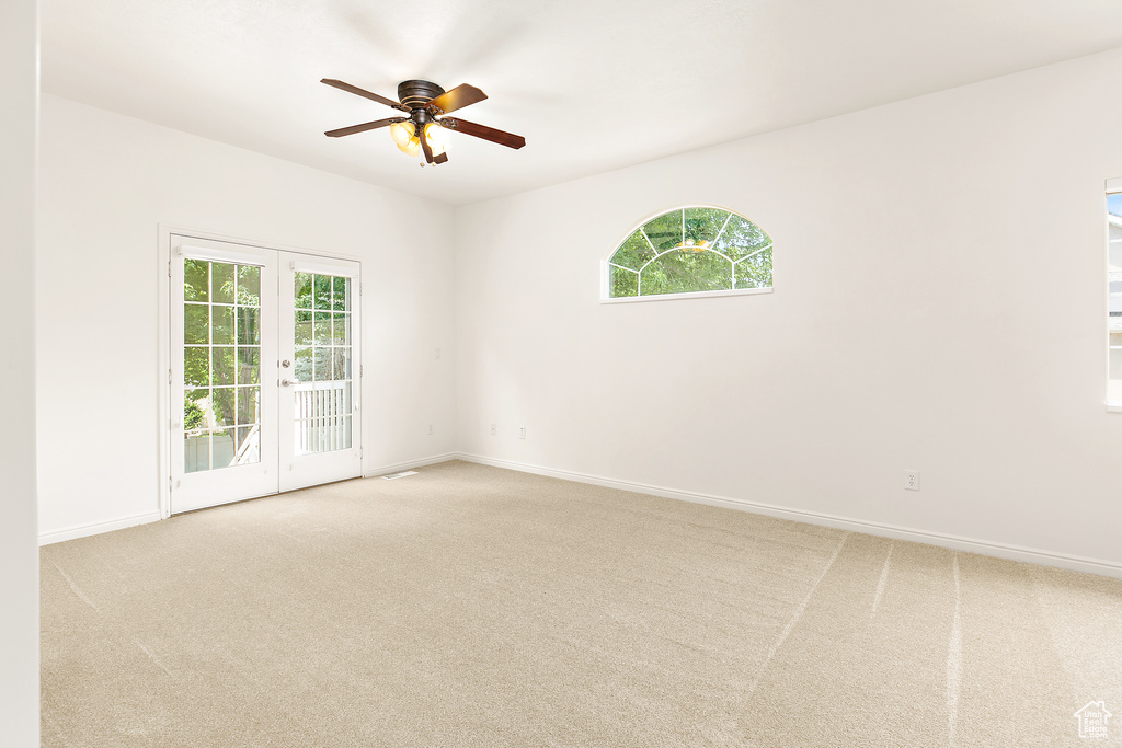 Carpeted spare room with french doors, a ceiling fan, and healthy amount of natural light