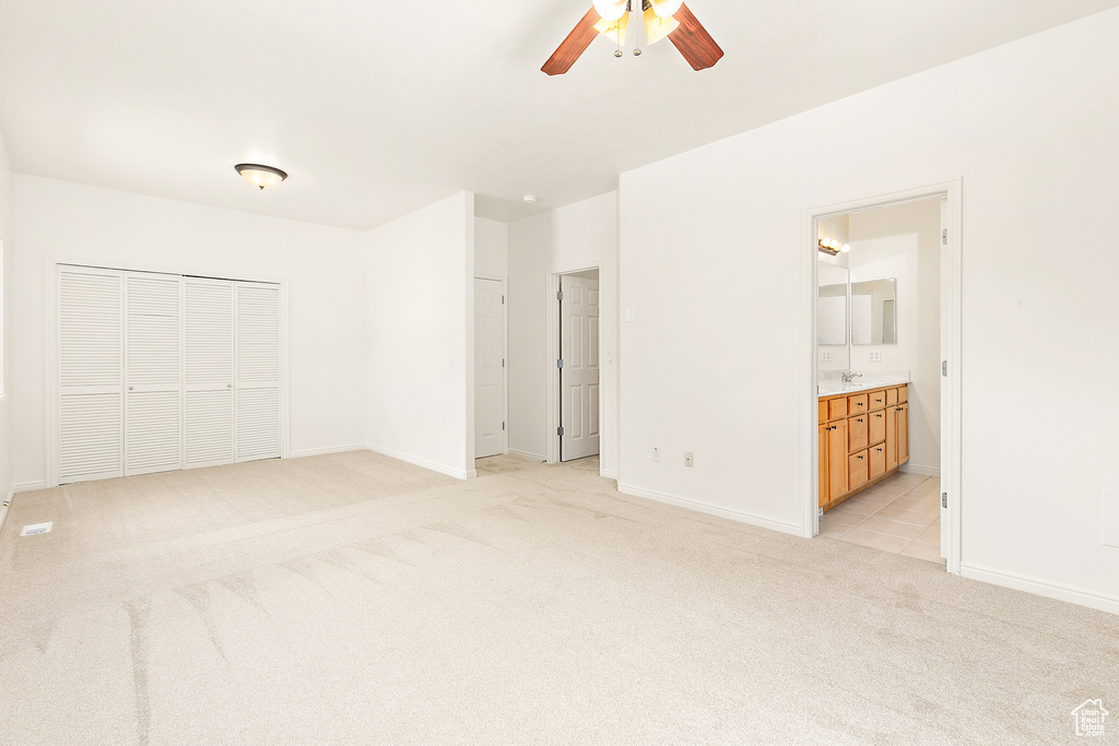Unfurnished bedroom with light carpet, a closet, ensuite bath, and ceiling fan