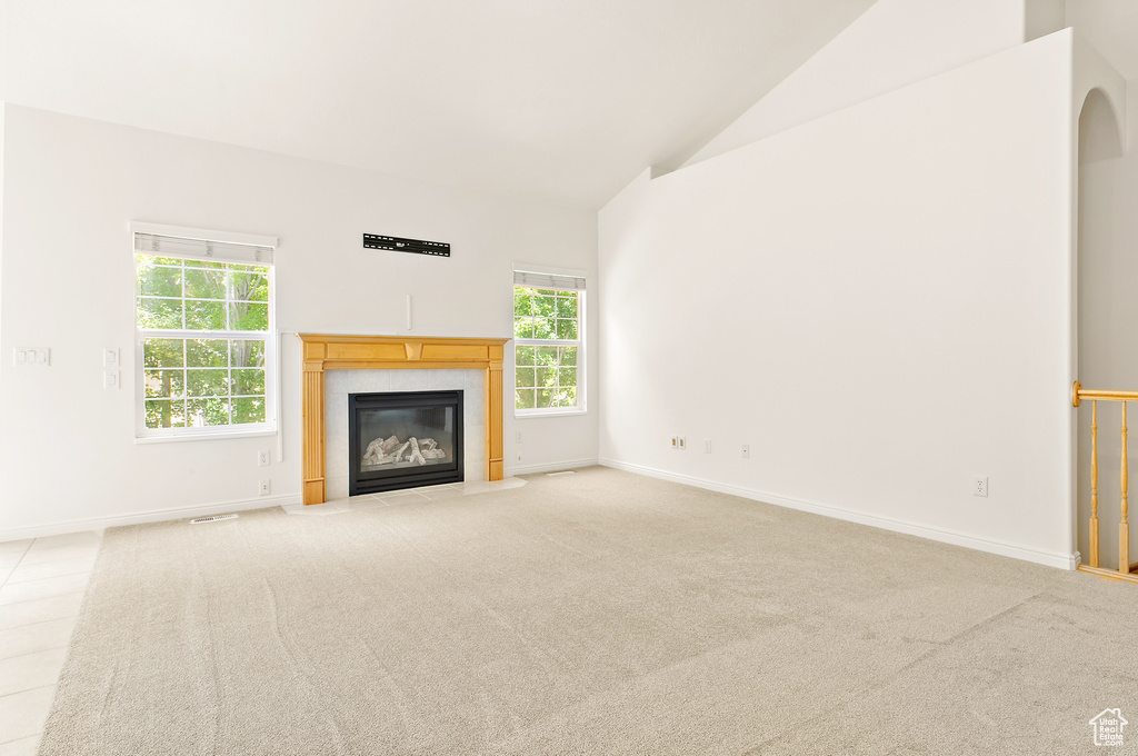 Unfurnished living room featuring healthy amount of natural light, a fireplace with flush hearth, light colored carpet, and high vaulted ceiling