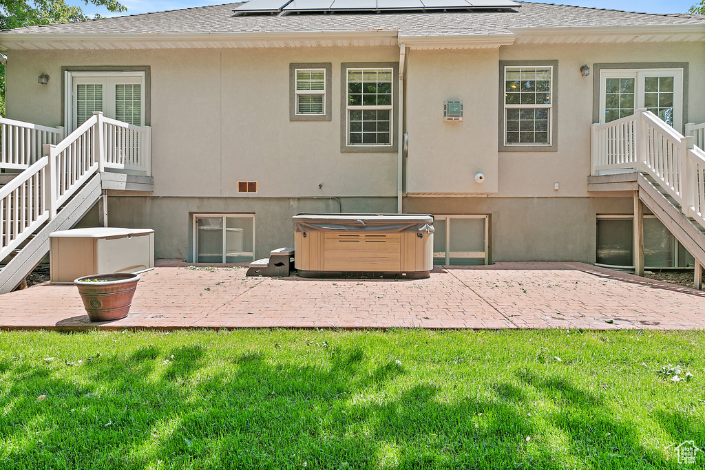 Back of property with a hot tub, a patio, and a yard