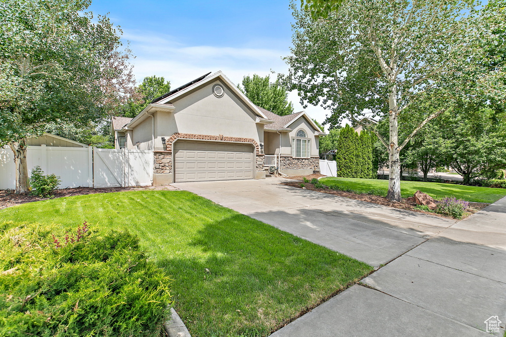 View of front facade with stucco siding, stone siding, a garage, concrete driveway, and a gate