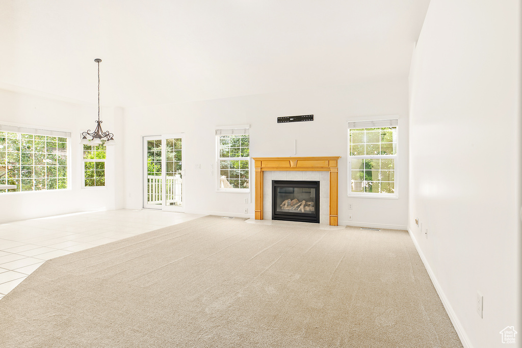 Unfurnished living room featuring a fireplace with flush hearth, a chandelier, light tile patterned floors, and light colored carpet