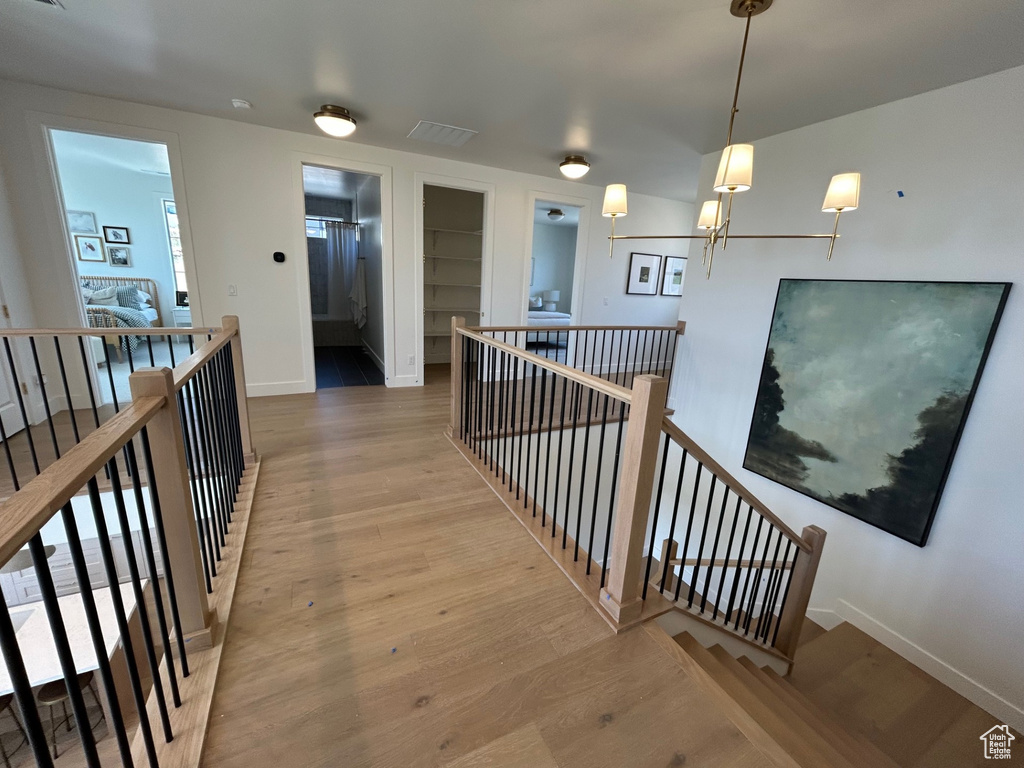 Hallway with an upstairs landing, built in shelves, wood finished floors, and a chandelier