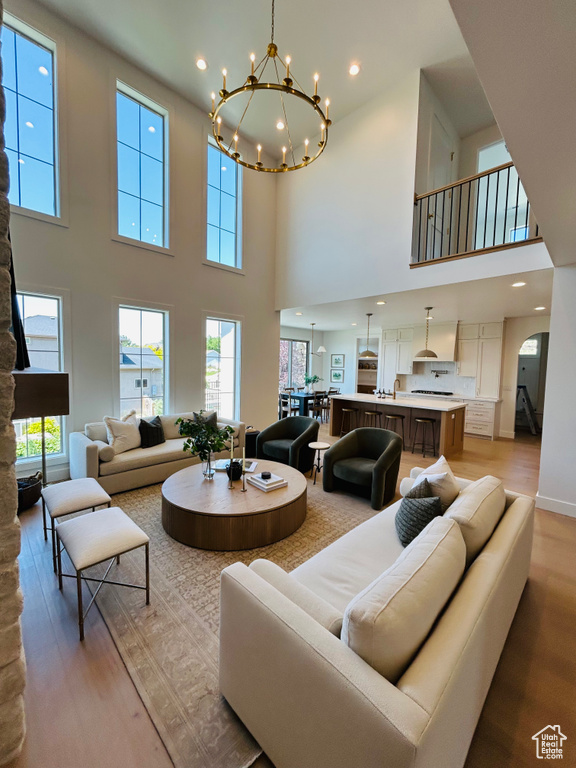 Living area with a towering ceiling, light wood-style flooring, plenty of natural light, a chandelier, and recessed lighting