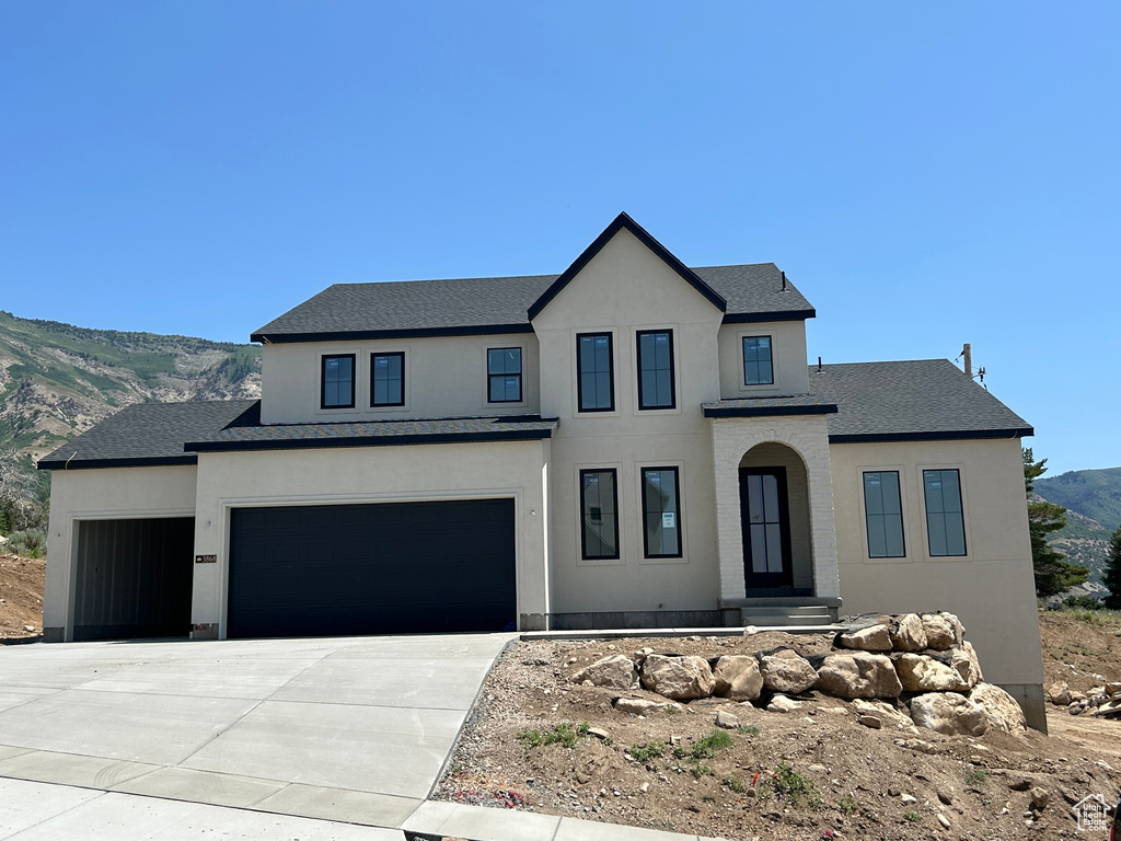 View of front facade with stucco siding, concrete driveway, a mountain view, a garage, and roof with shingles