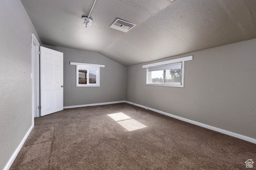Additional living space featuring vaulted ceiling, carpet flooring, a textured ceiling, and a textured wall