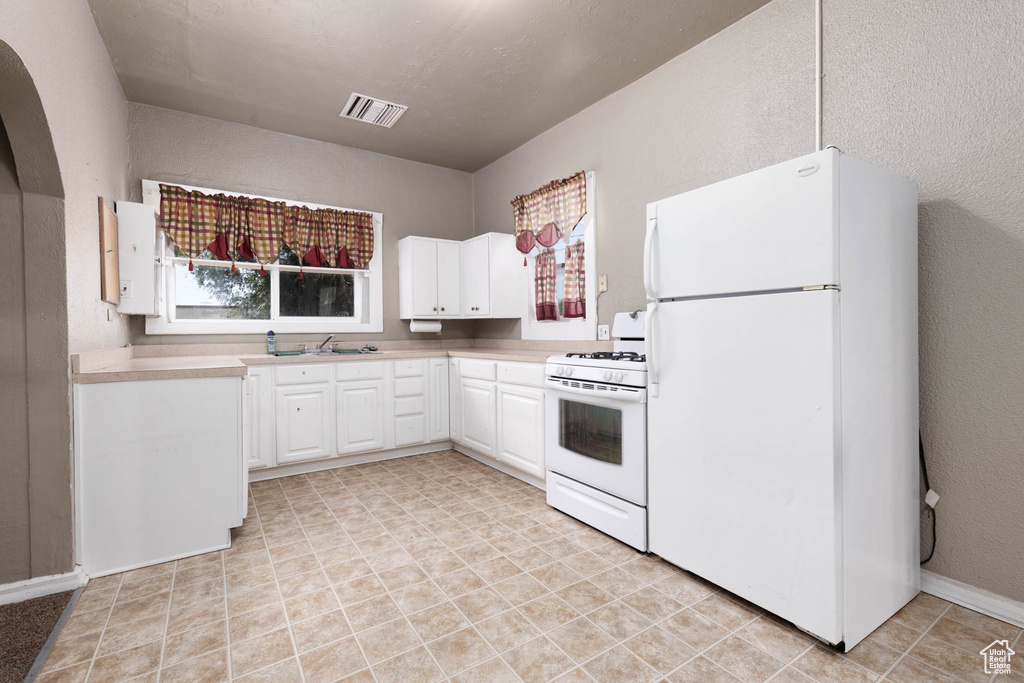 Kitchen with white appliances, white cabinetry, light countertops, arched walkways, and a textured wall