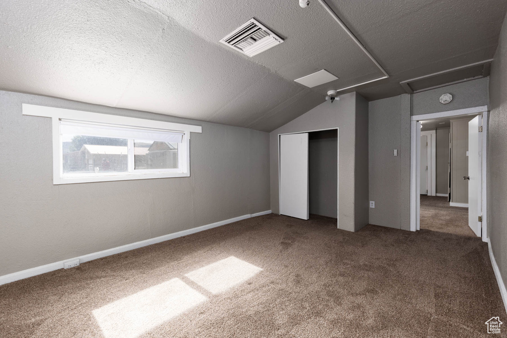 Unfurnished bedroom featuring a textured ceiling, carpet, lofted ceiling, and a closet