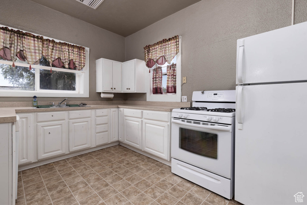 Kitchen with white appliances, light countertops, white cabinets, and light floors