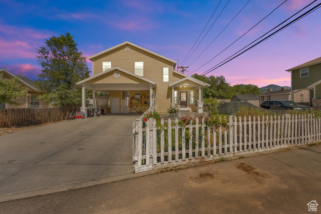 Traditional home with covered porch, a carport, driveway, and a fenced front yard