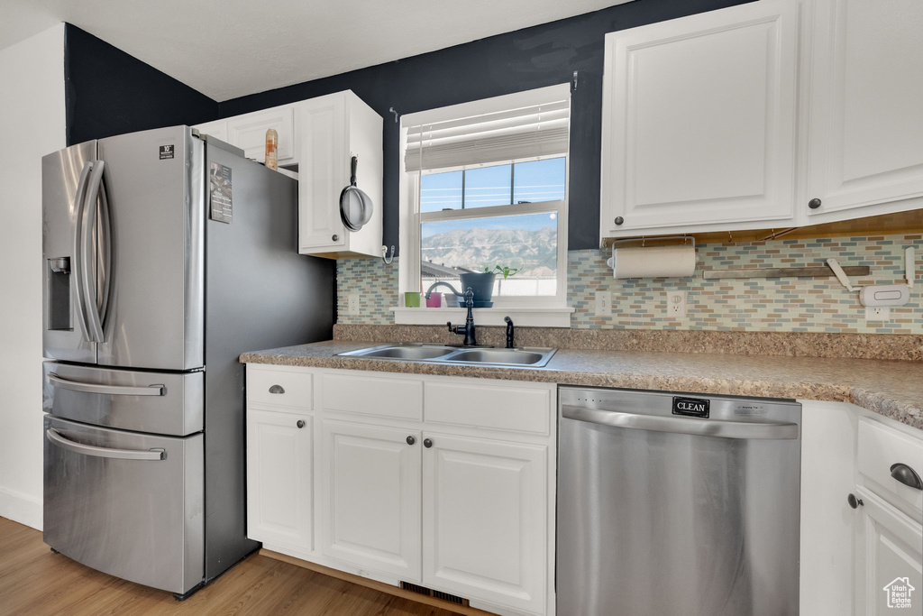 Kitchen with stainless steel appliances, light wood-style flooring, white cabinetry, and decorative backsplash