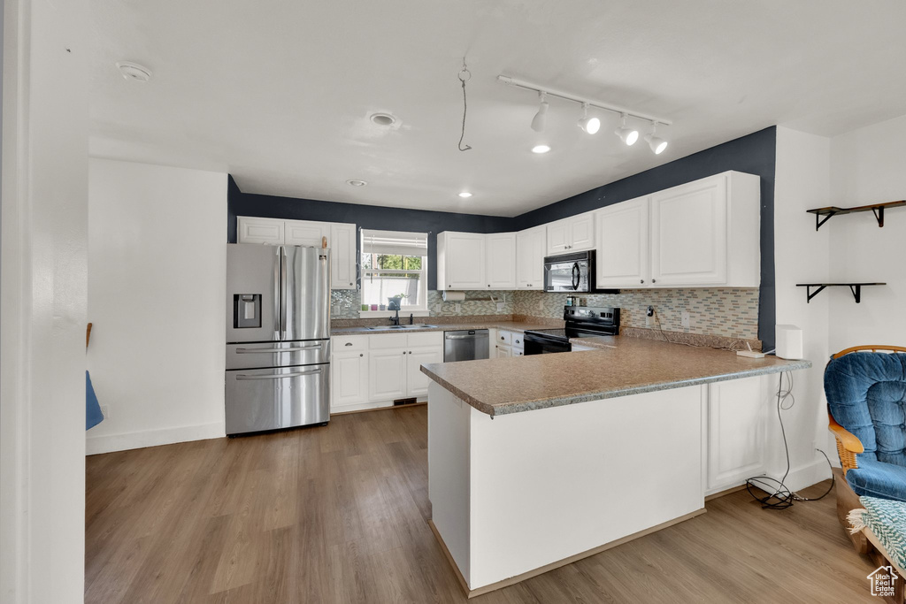 Kitchen with black appliances, a peninsula, white cabinets, and wood finished floors