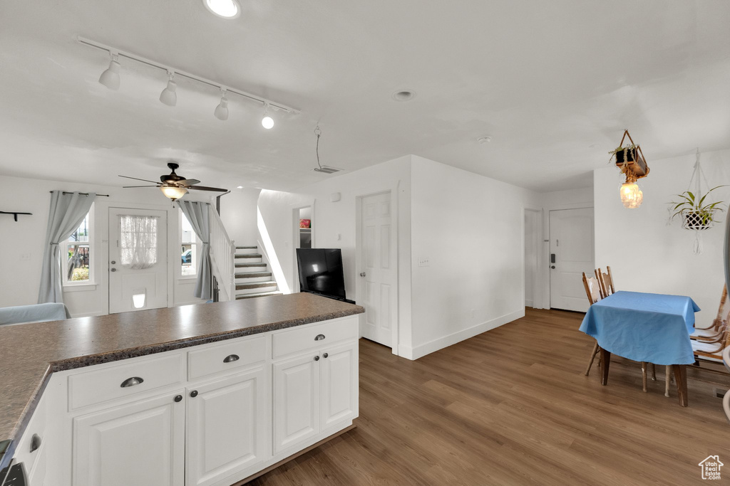 Kitchen with dark countertops, a ceiling fan, wood finished floors, white cabinets, and track lighting