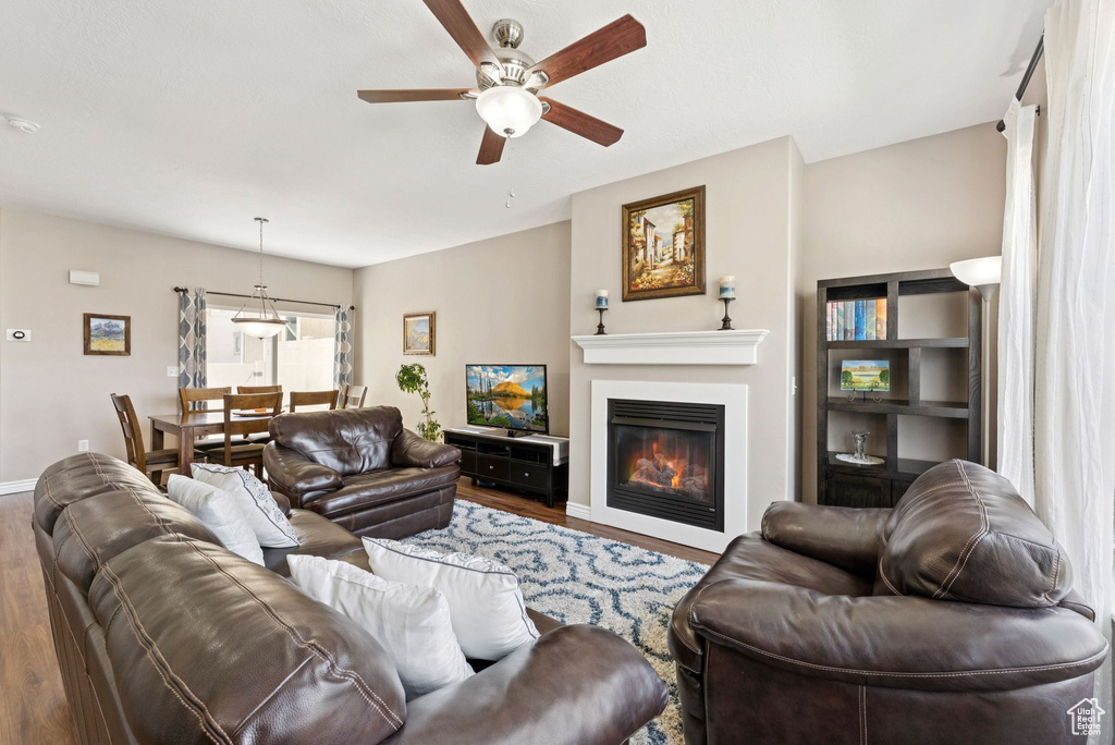 Living room with wood finished floors, a ceiling fan, and a glass covered fireplace