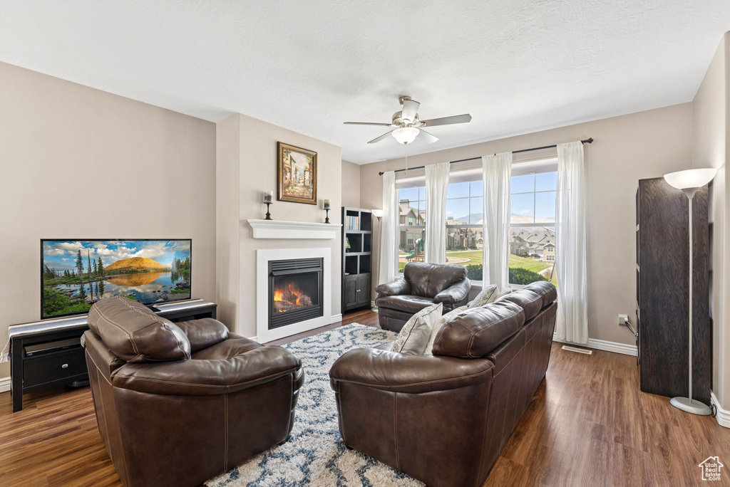 Living room with wood finished floors, ceiling fan, and a glass covered fireplace