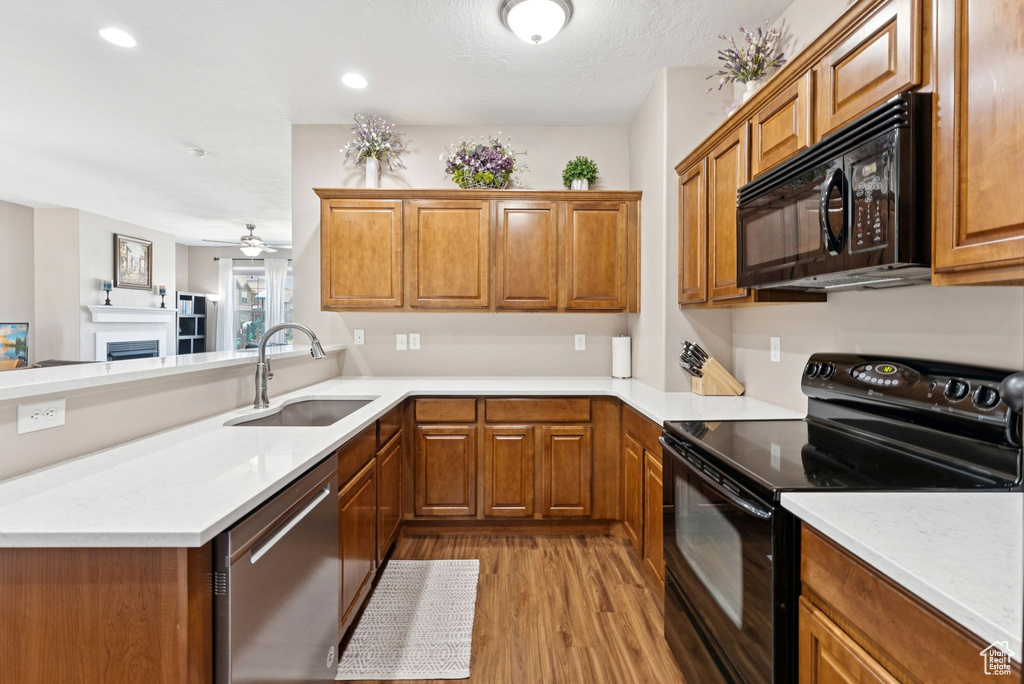 Kitchen featuring black appliances, wood finished floors, brown cabinetry, a peninsula, and recessed lighting